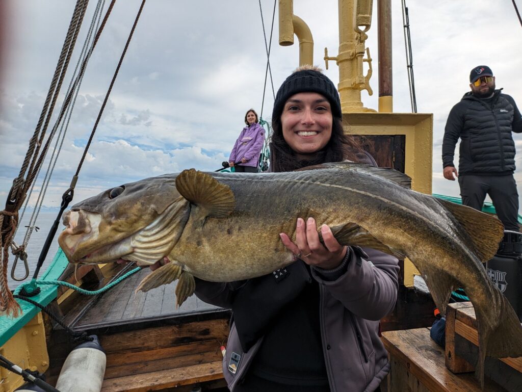 Kvinne på fisketur i Lofoten holder en stor torsk ombord i båten.