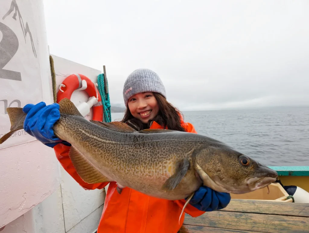 Young woman proudly holding a freshly caught Lofoten cod during a fishing trip in Norway